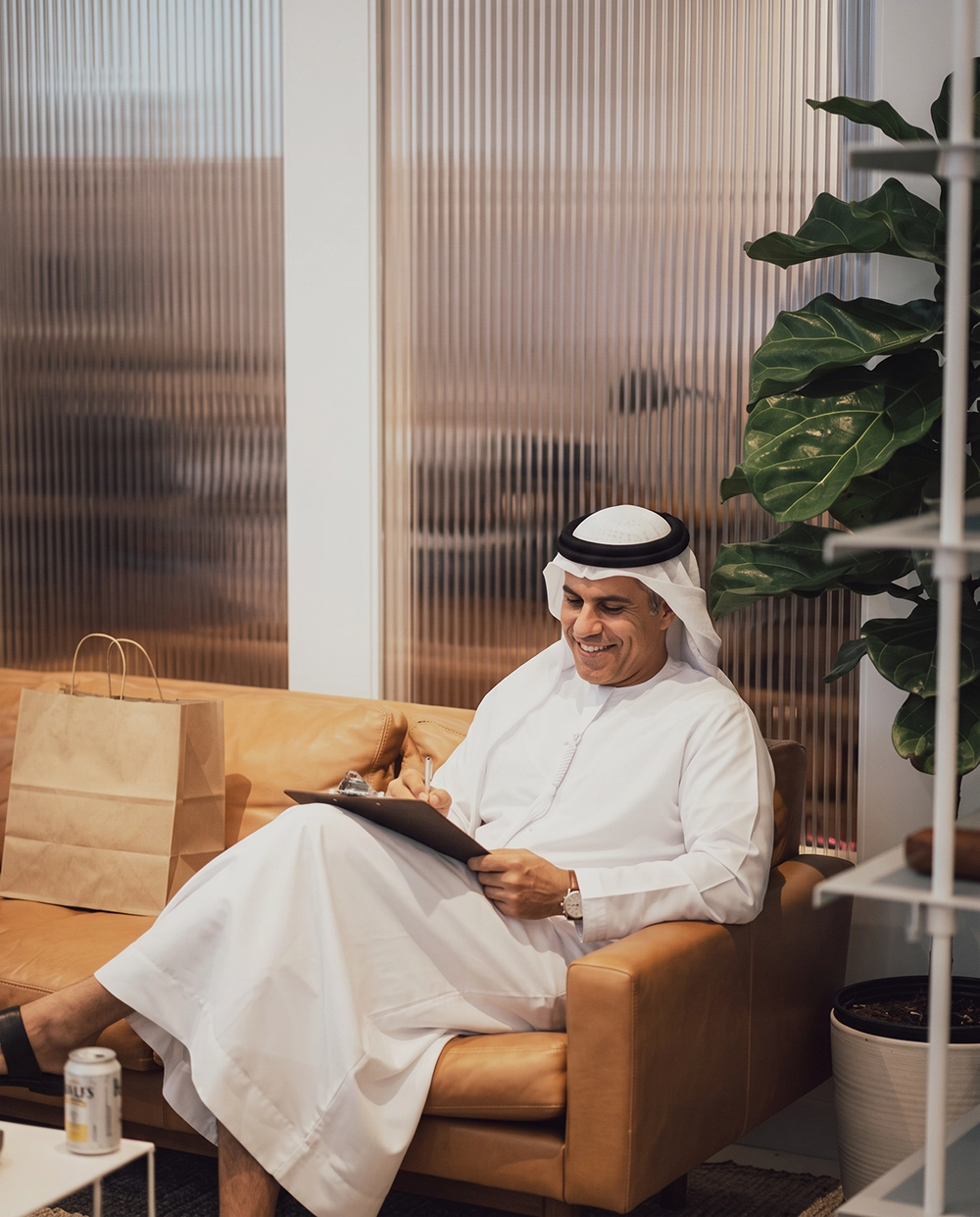 A relaxed Emirati man sitting on a leather couch reviewing wealth management strategies on a clipboard to achieve the best financial outcomes.